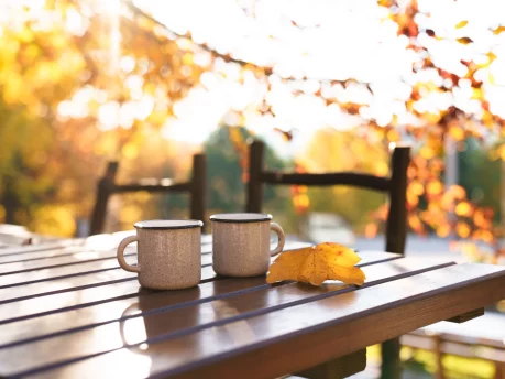 Two mugs on a wooden table surrounded by autumn trees
